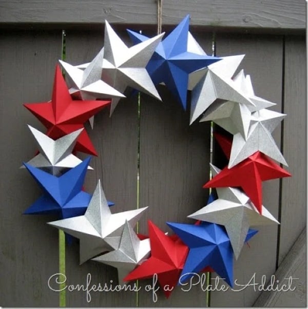 Red, white, and blue paper star wreath hanging on dark wood fence for patriotic front door decor