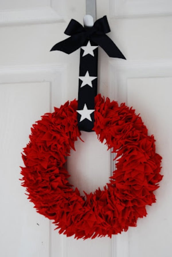 Red felt patriotic wreath hanging on white door with navy ribbon and white star accents