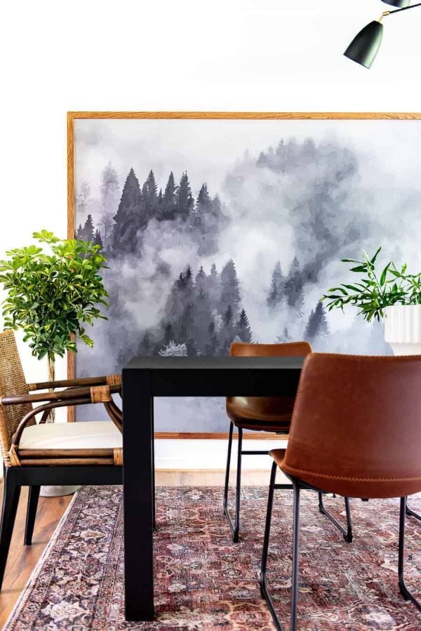 Large painted forest landscape framed with wood trim to resemble oversized artwork above a dining room table.
