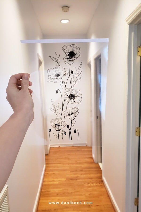 Hand tracing a floral design onto a white wall using a clear template before painting an easy DIY wall mural.