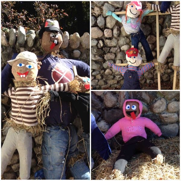 Colorful homemade scarecrows in playful outfits displayed outdoors against a stone wall.