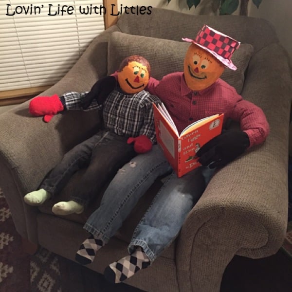 Two homemade paper mache scarecrows sitting together in a chair and reading a book.